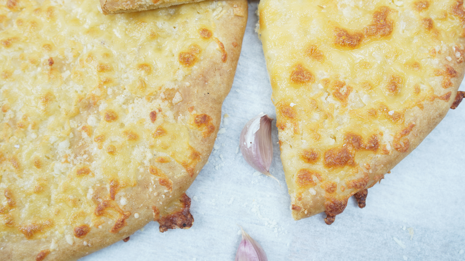 Close-up of two garlic cheese bread slices showing browned cheese and crisp edges