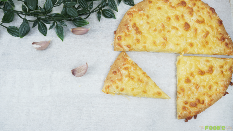 Baked garlic cheese bread cut into slices on parchment paper with garlic cloves nearby