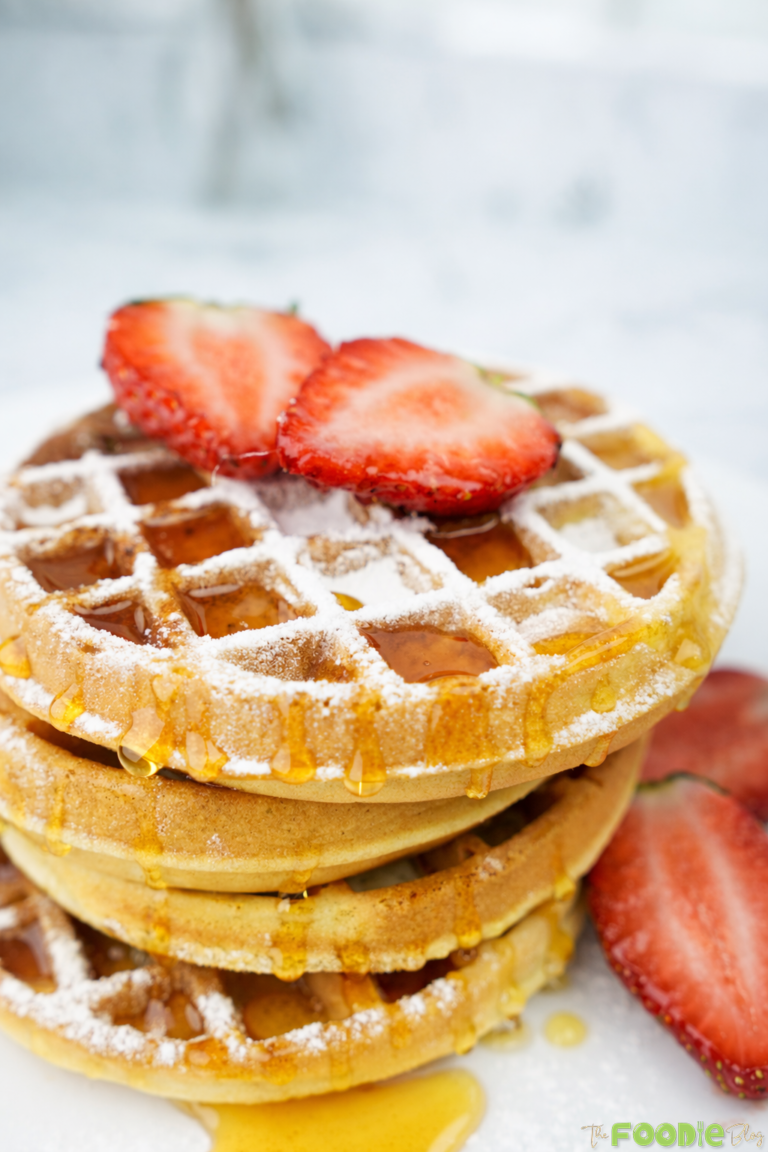 Stack of waffles topped with strawberries and syrup on a white plate