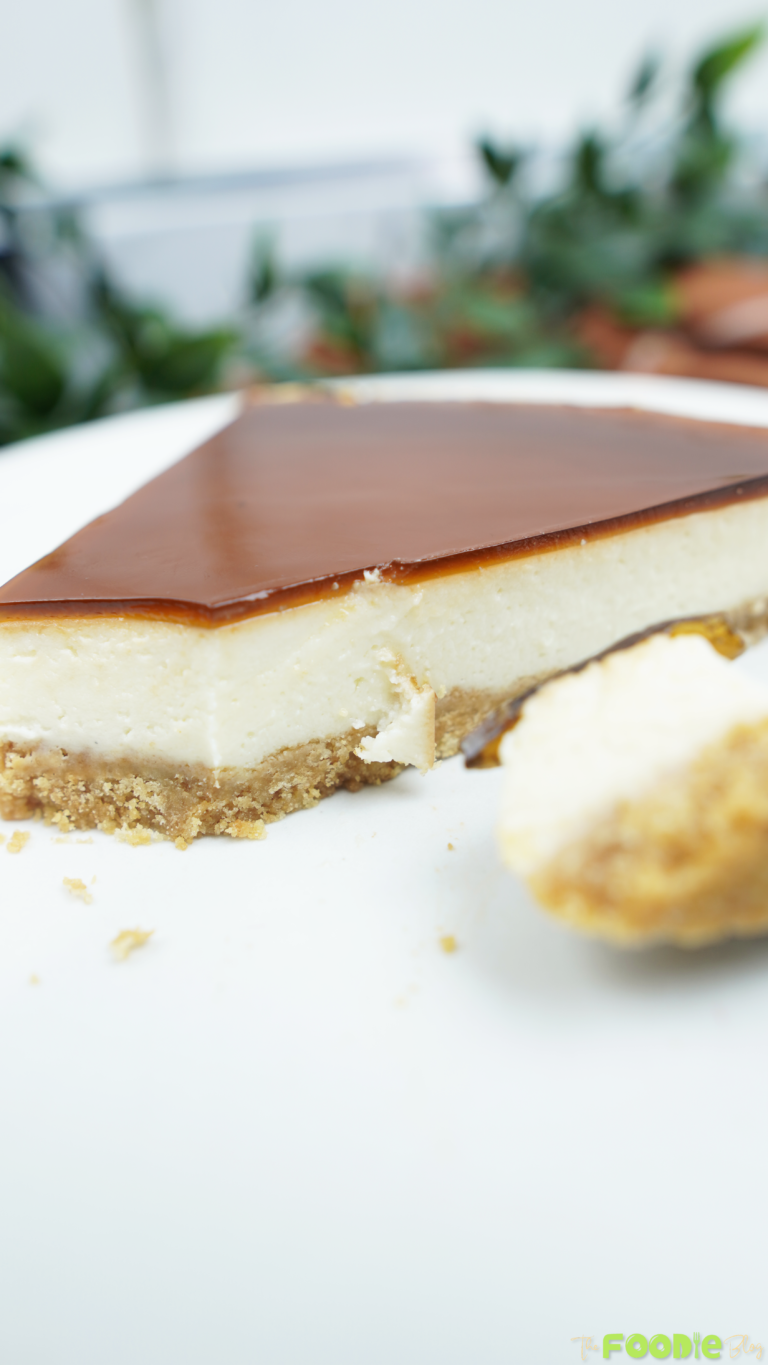 Close-up of a yogurt cheesecake slice with a glossy caramel coffee topping and biscuit crust on a white plate