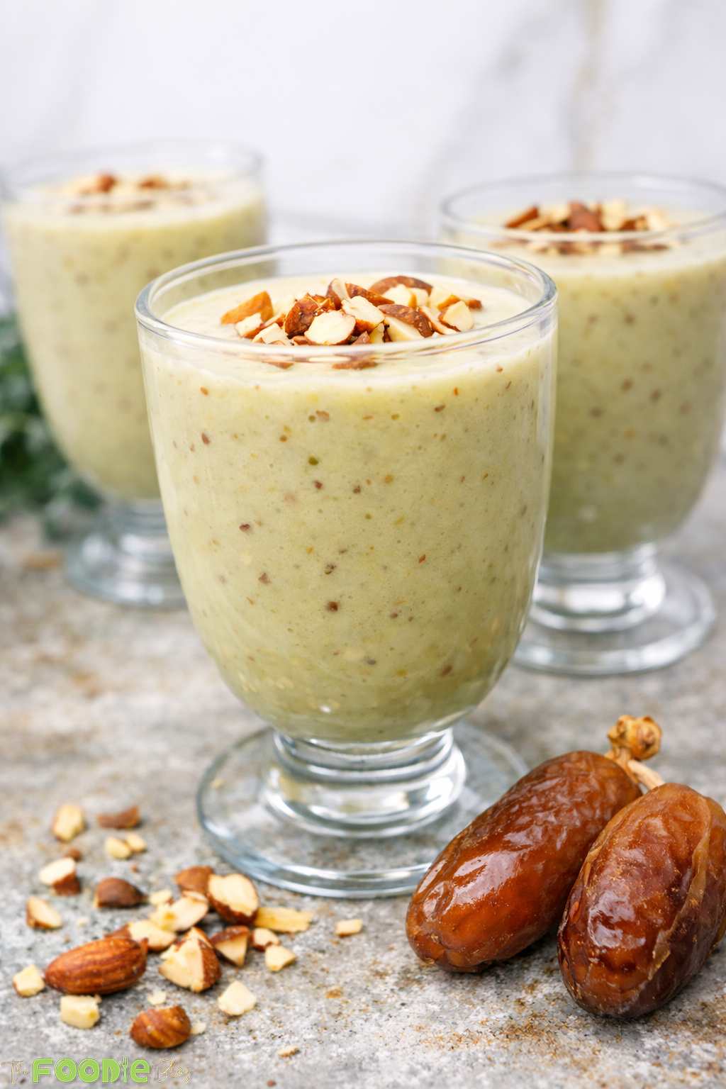 Avocado date almond drink smoothie with almonds and dates beside the glass