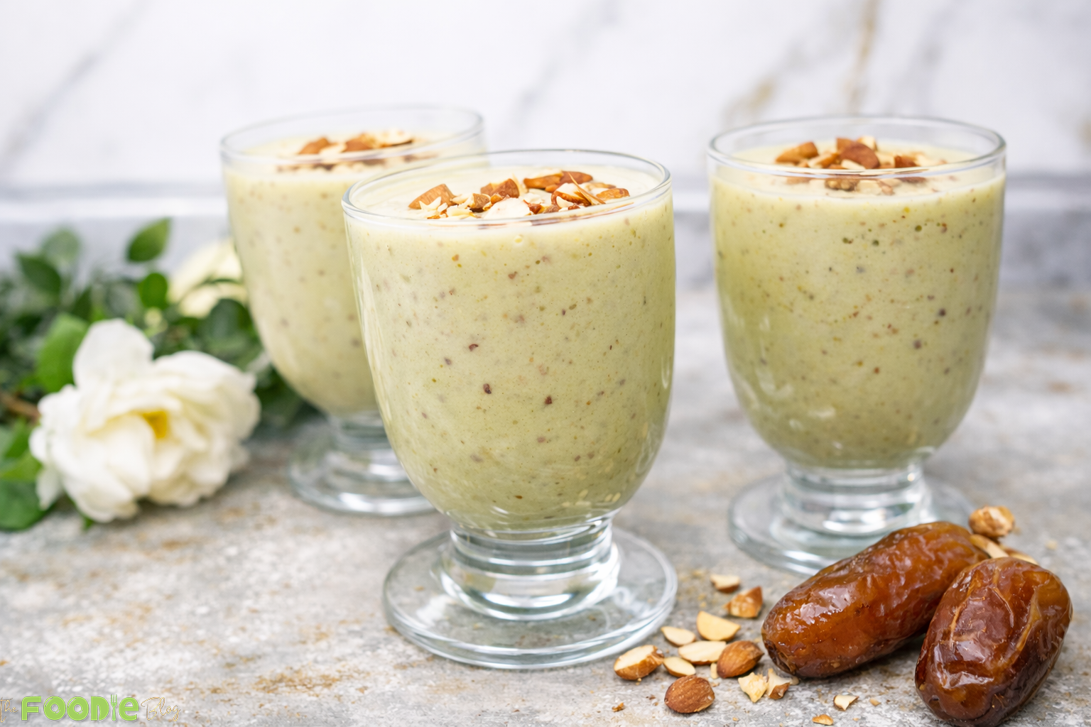 Avocado date almond drink smoothie with almonds and dates beside the glass