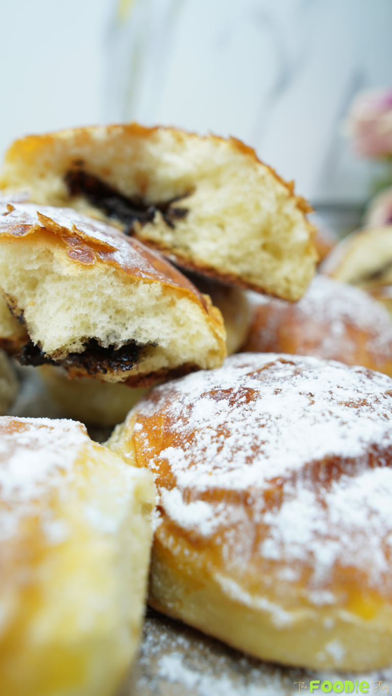 Brioche with chocolate filling stacked over powdered sugar–dusted buns in the background