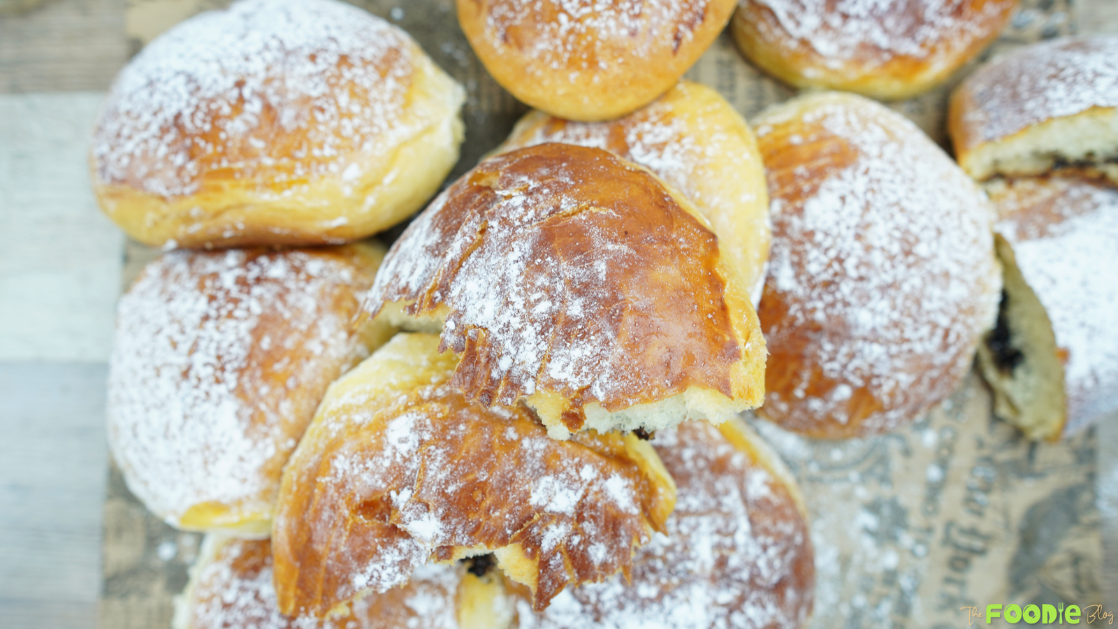 Powdered sugar–dusted brioche buns stacked on a board, with one bun split to show chocolate filling