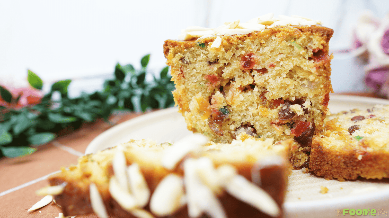 Candied fruit cake loaf with apricot glaze, studded with raisins and colorful candied fruit on a plate.