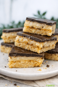 Close-up of caramel slice bars with a thick caramel layer and smooth chocolate topping on a plate.