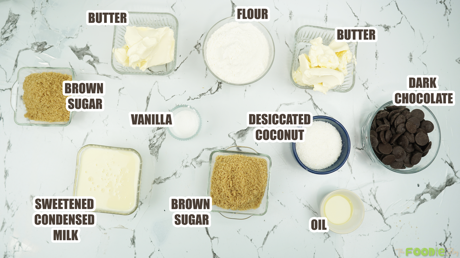 Overhead view of labeled caramel slice ingredients on a white marble counter
