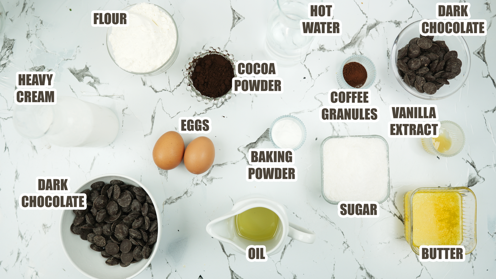 Overhead view of chocolate fudge cake ingredients labeled on a marble surface