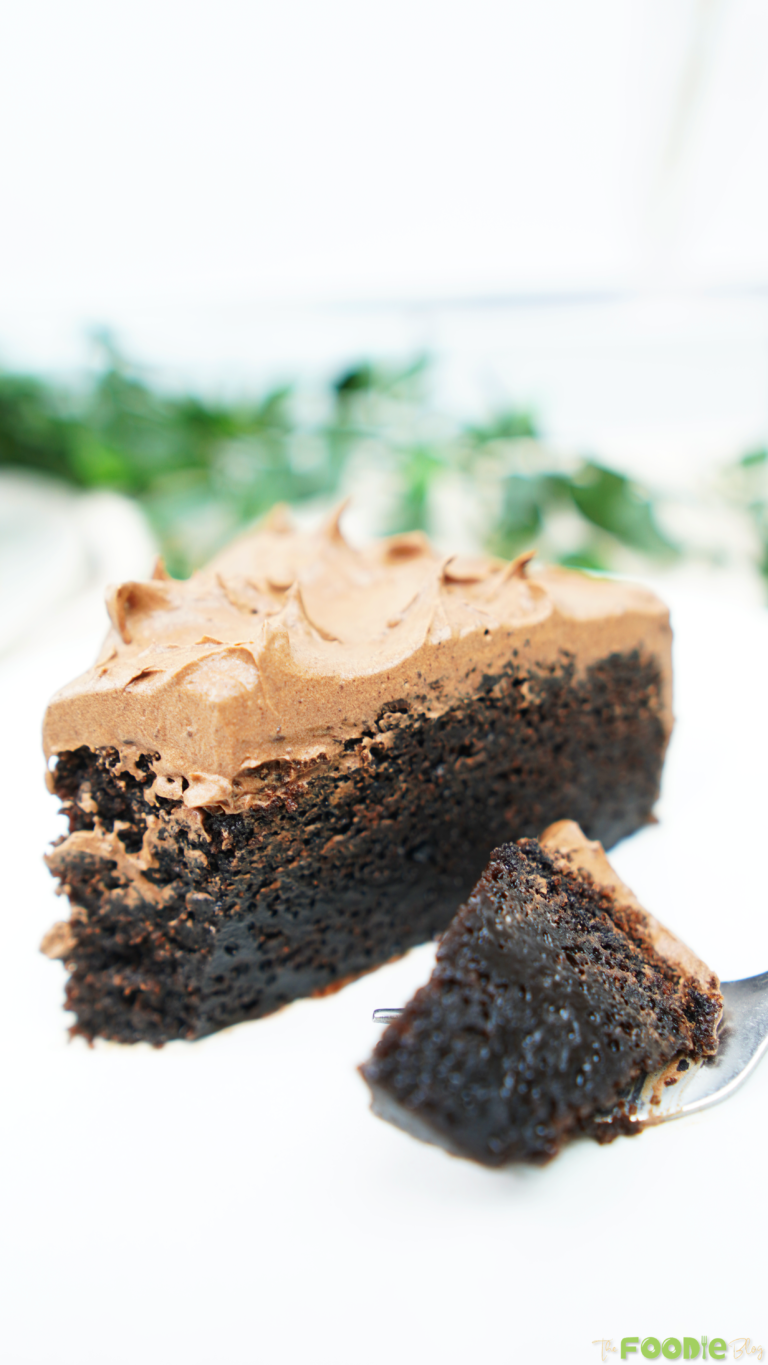 Fork holding a bite of Chocolate Fudge Cake with chocolate ganache frosting in the background.