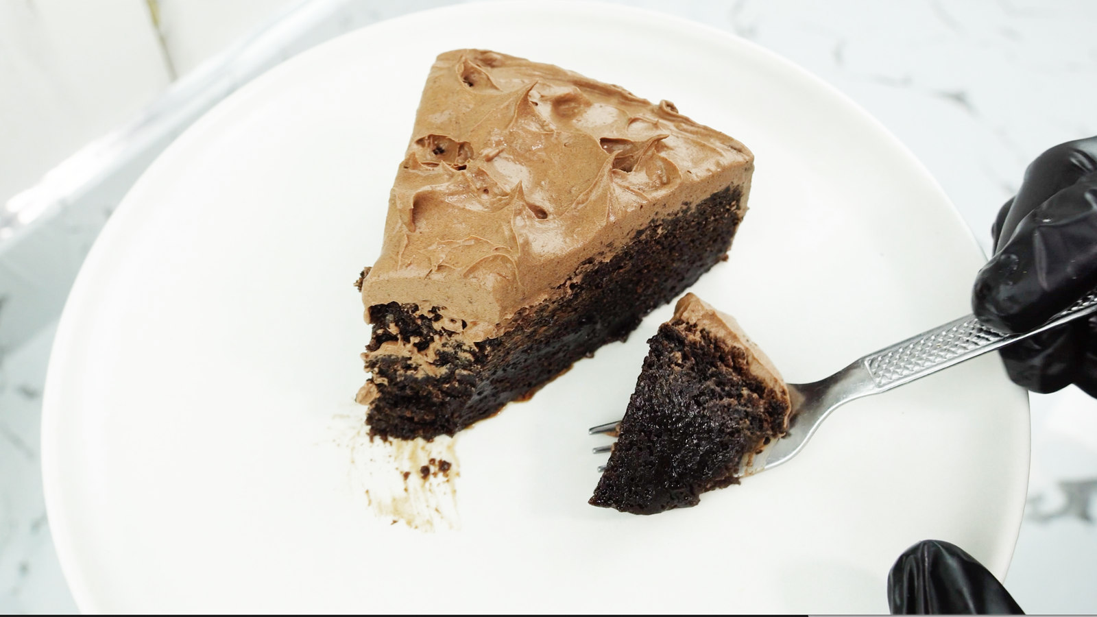 Chocolate fudge cake slice on a white plate with a fork holding a bite