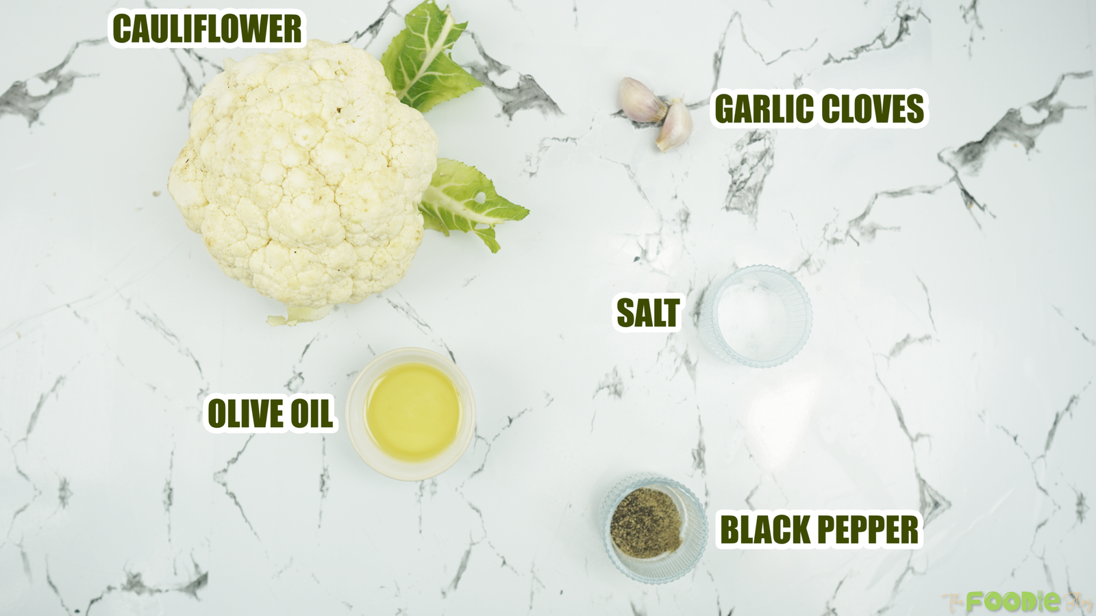 Cauliflower, olive oil, garlic cloves, salt, and black pepper on a marble surface