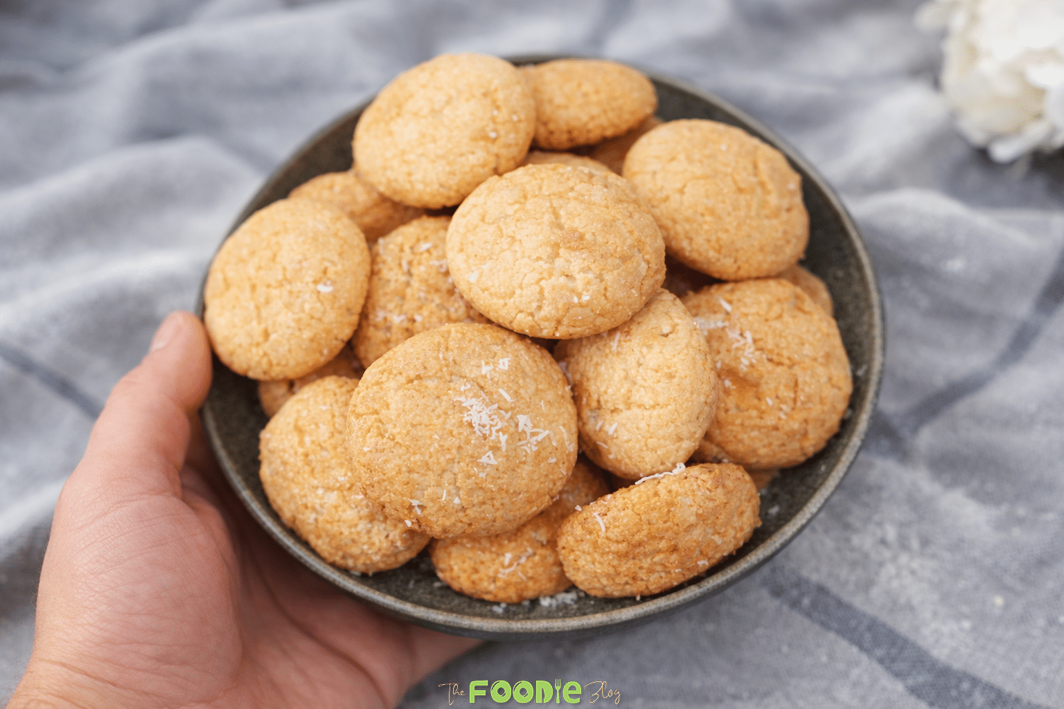 Bowl of coconut macaroons held by hand, showing small golden cookies with shredded coconut on top.