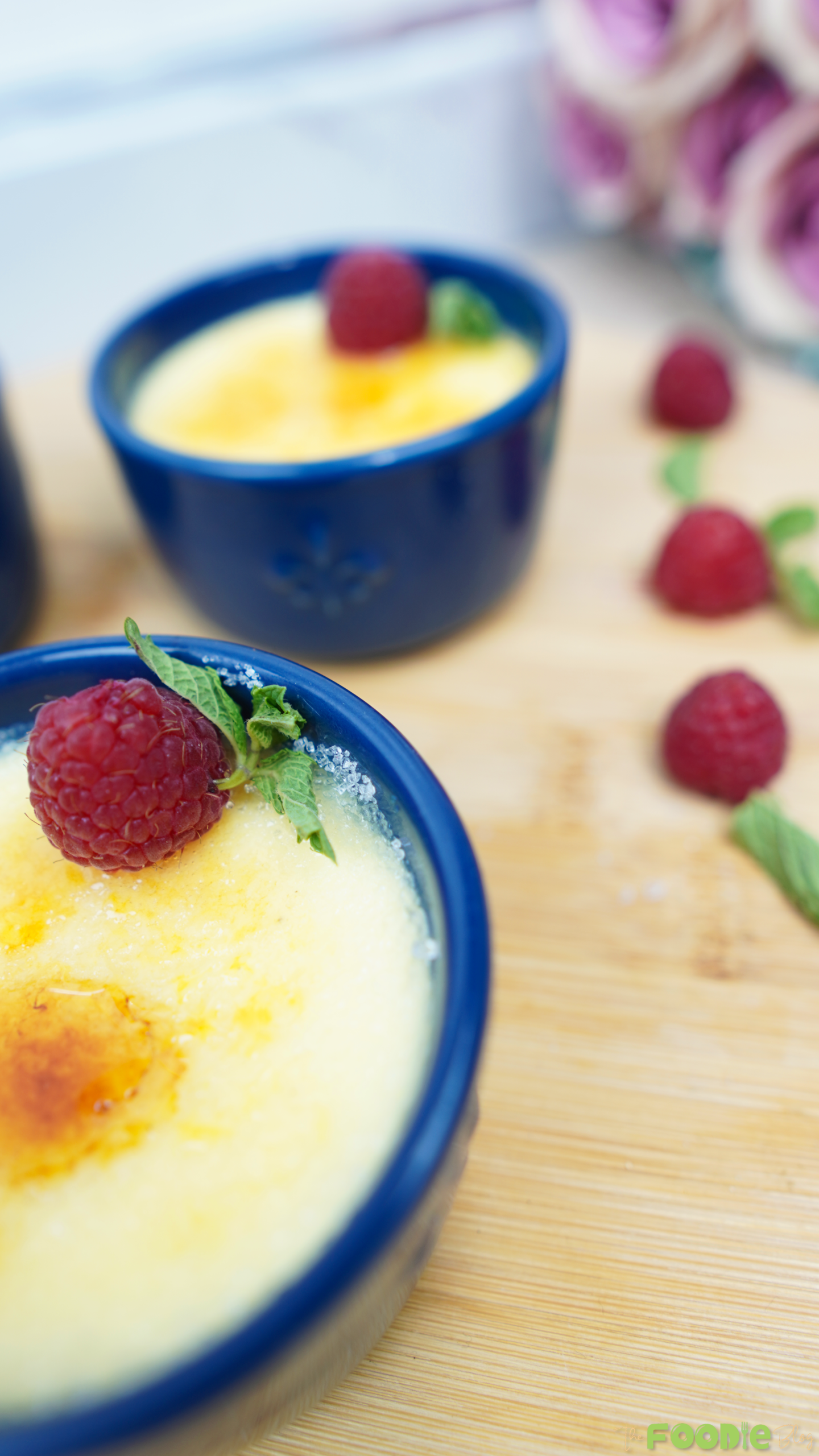 Close-up creme brulee in a blue ramekin topped with a raspberry and mint