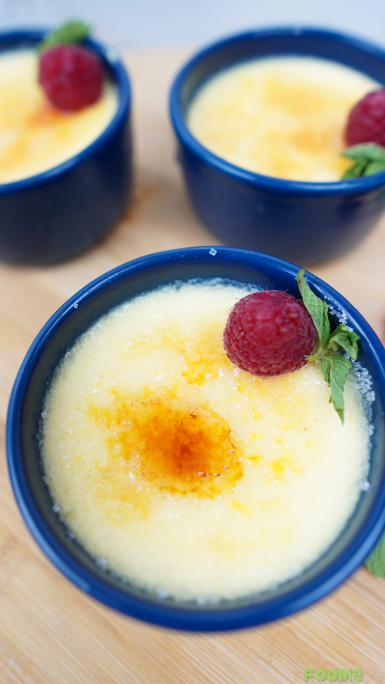 Creme brulee with a caramelized sugar top in a blue ramekin, garnished with a raspberry and mint