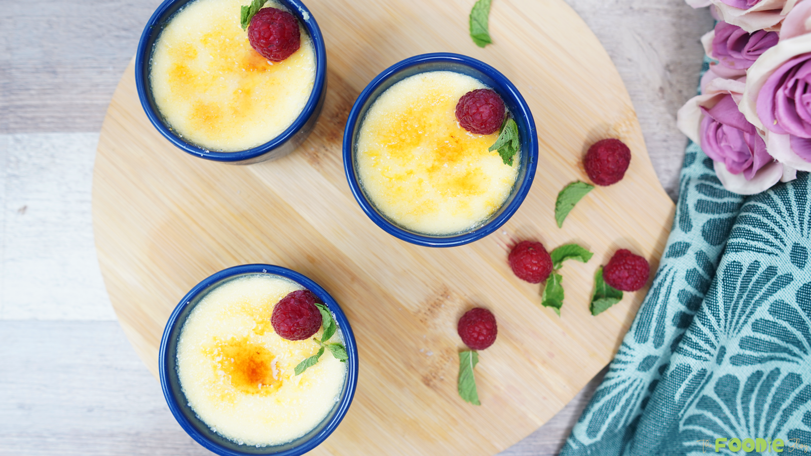 Overhead view of three creme brulee ramekins with raspberries and mint on a wooden board