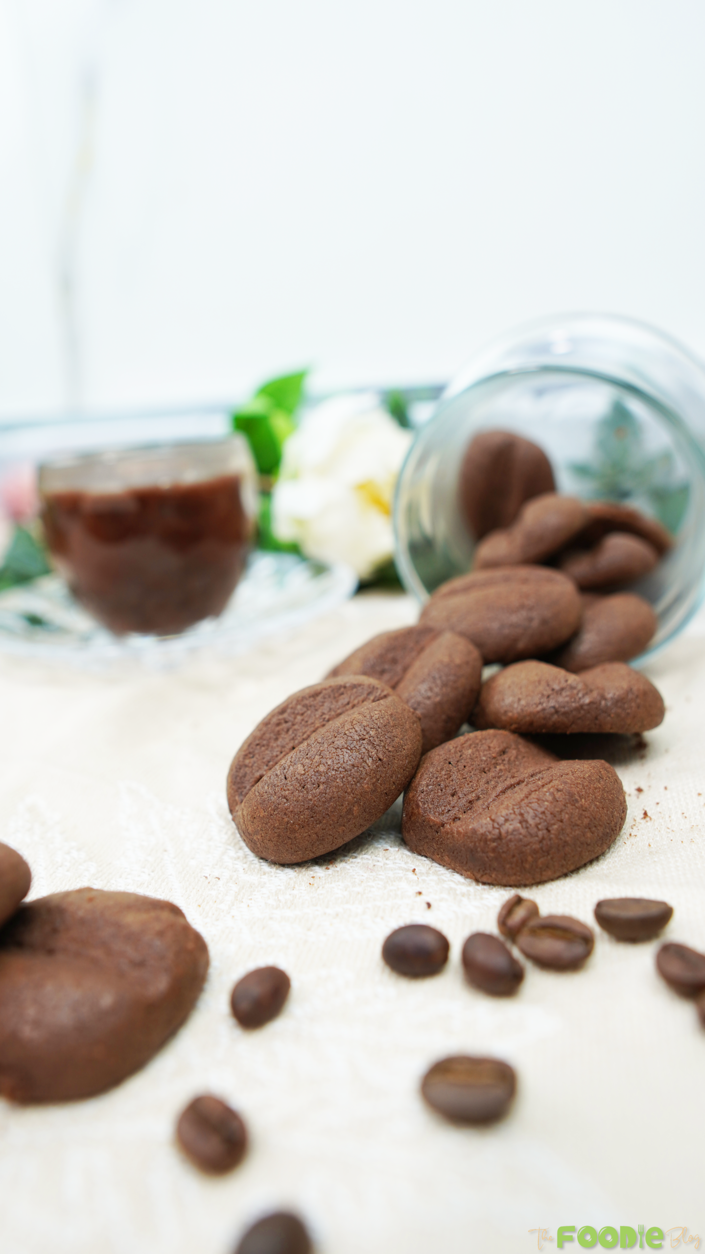 Close-up of Crispy Coffee Biscuits scattered on a light cloth with coffee beans in front