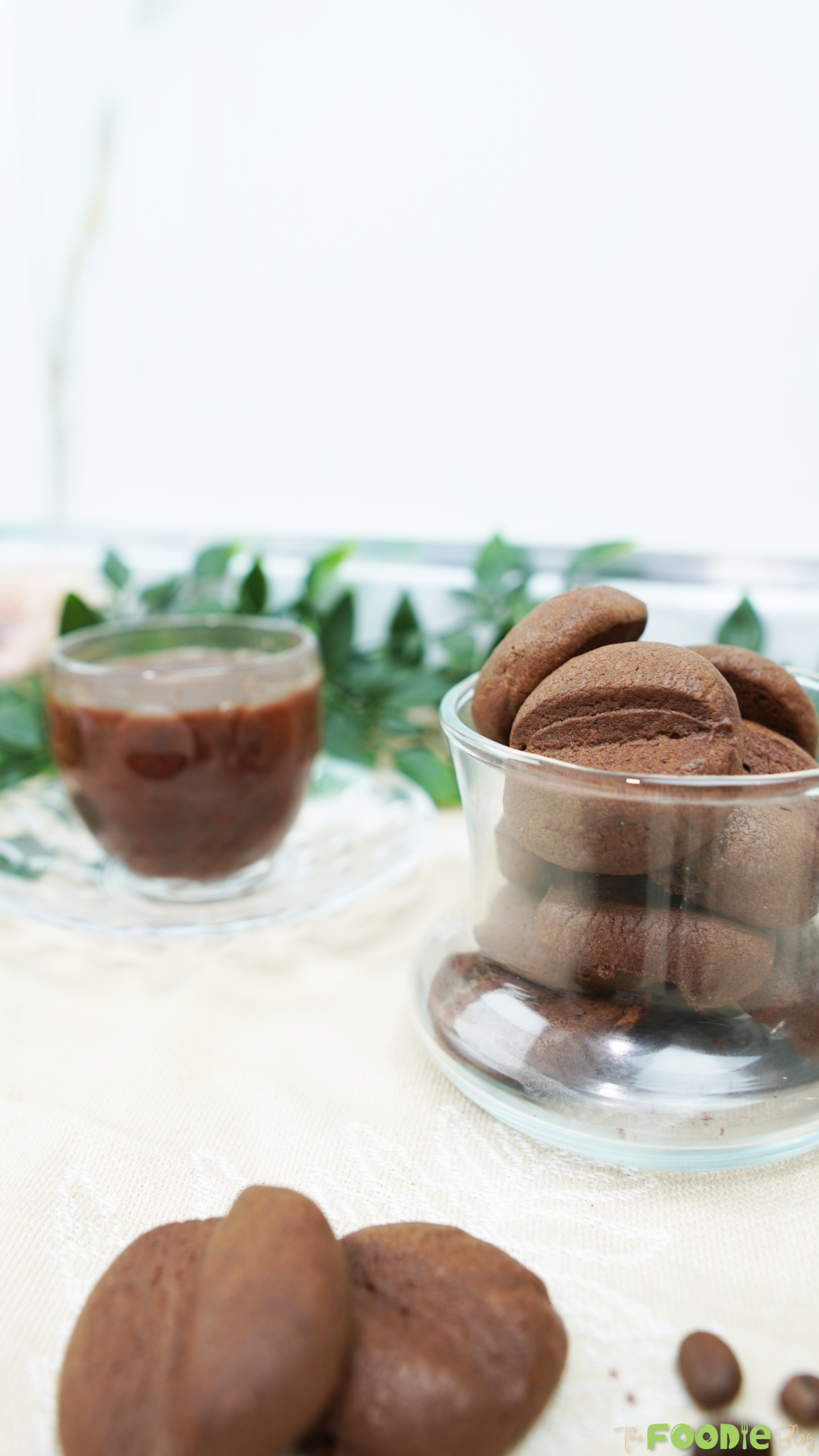Crispy Coffee Biscuits stacked in a clear glass bowl with a coffee cup in the background