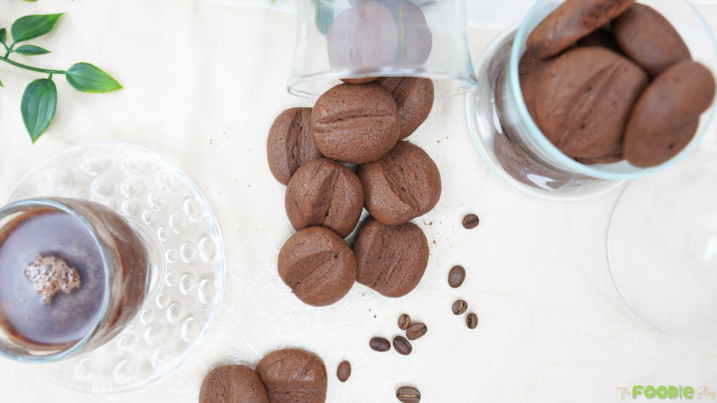 Overhead shot of Crispy Coffee Biscuits with a coffee cup, scattered coffee beans, and cookies in glass jars
