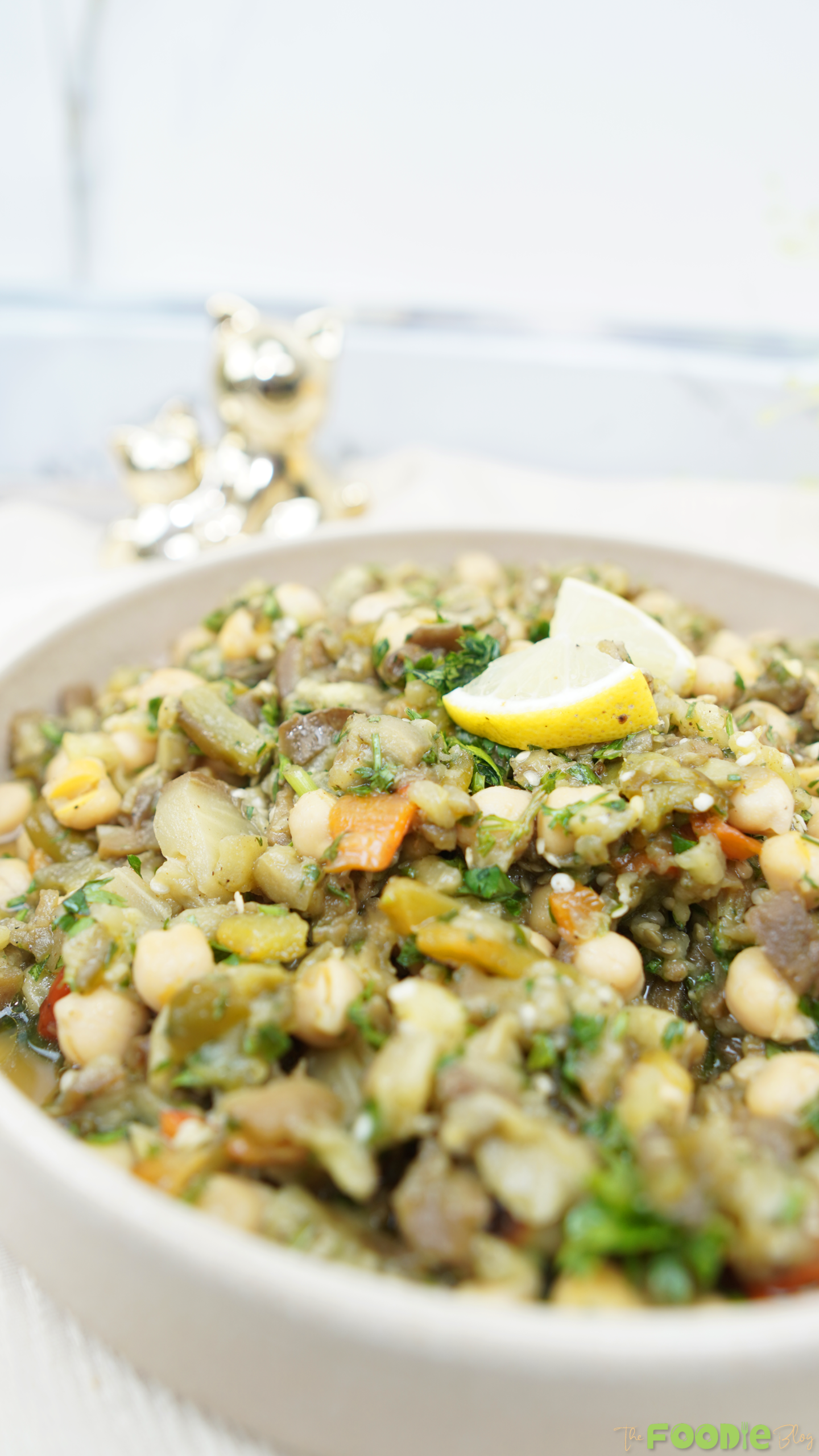 Close-up view of chunky roasted eggplant chickpea salad with herbs in a beige bowl