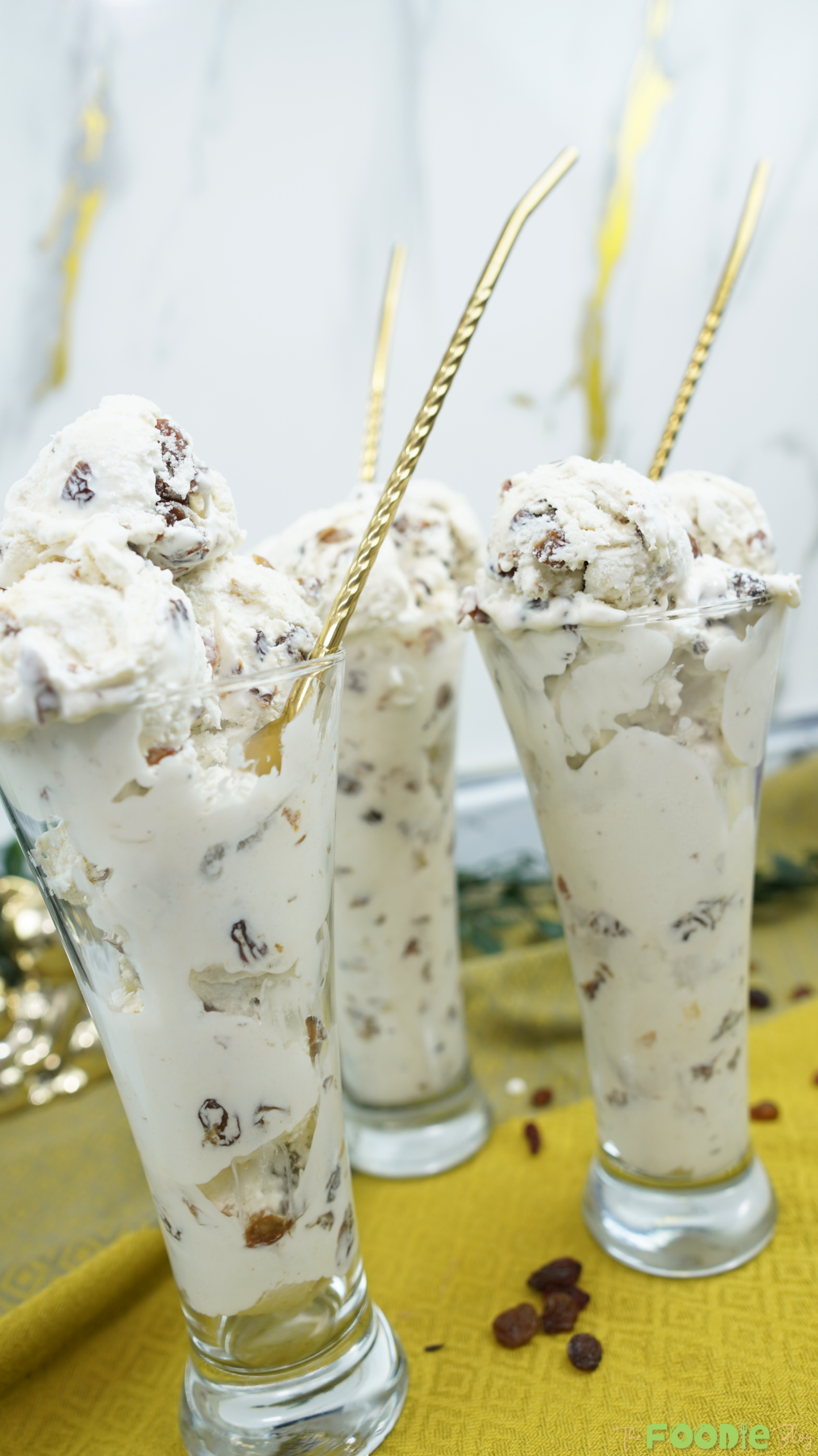 Three glasses of Easy Rum Ice Cream with raisins and gold spoons on a serving table