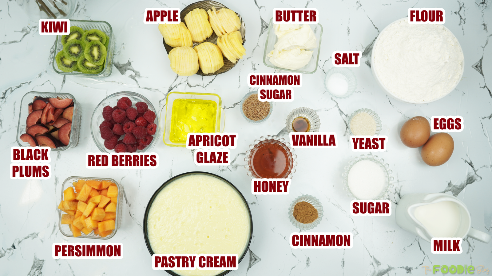 Overhead layout of ingredients for fruit brioche, including flour, milk, eggs, yeast, butter, honey, pastry cream, and fresh fruit.