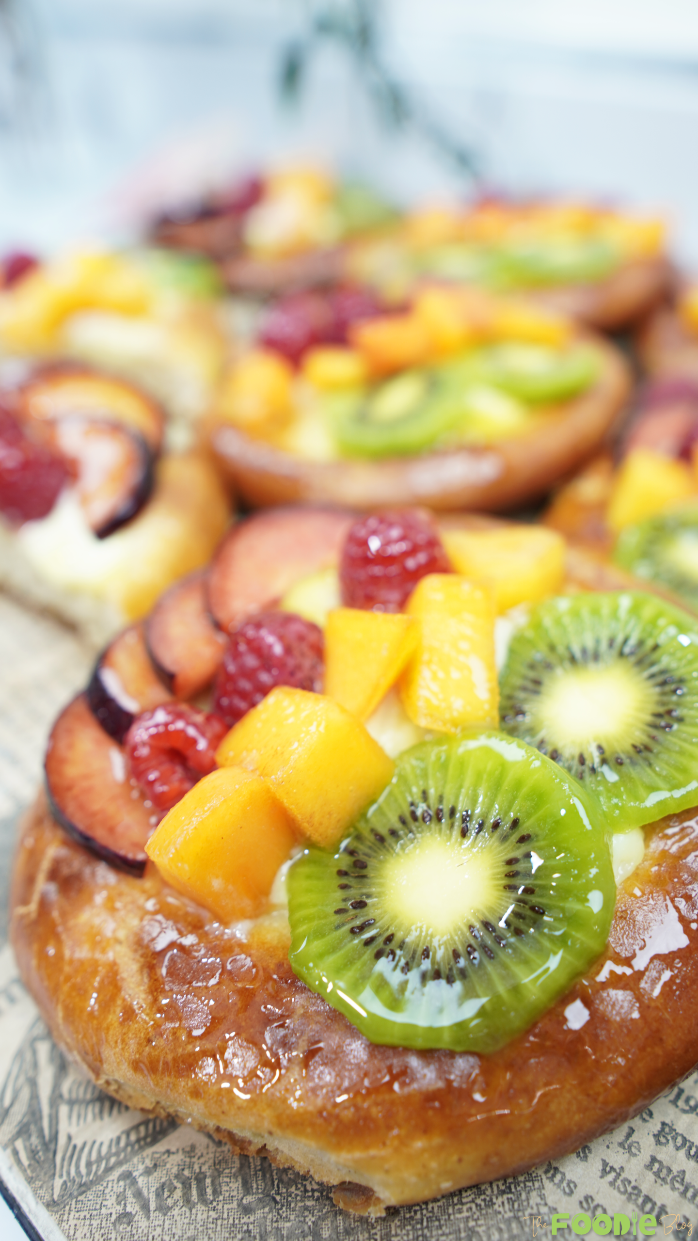 Close-up of a glazed brioche topped with pastry cream, kiwi slices, plum slices, and red berries.