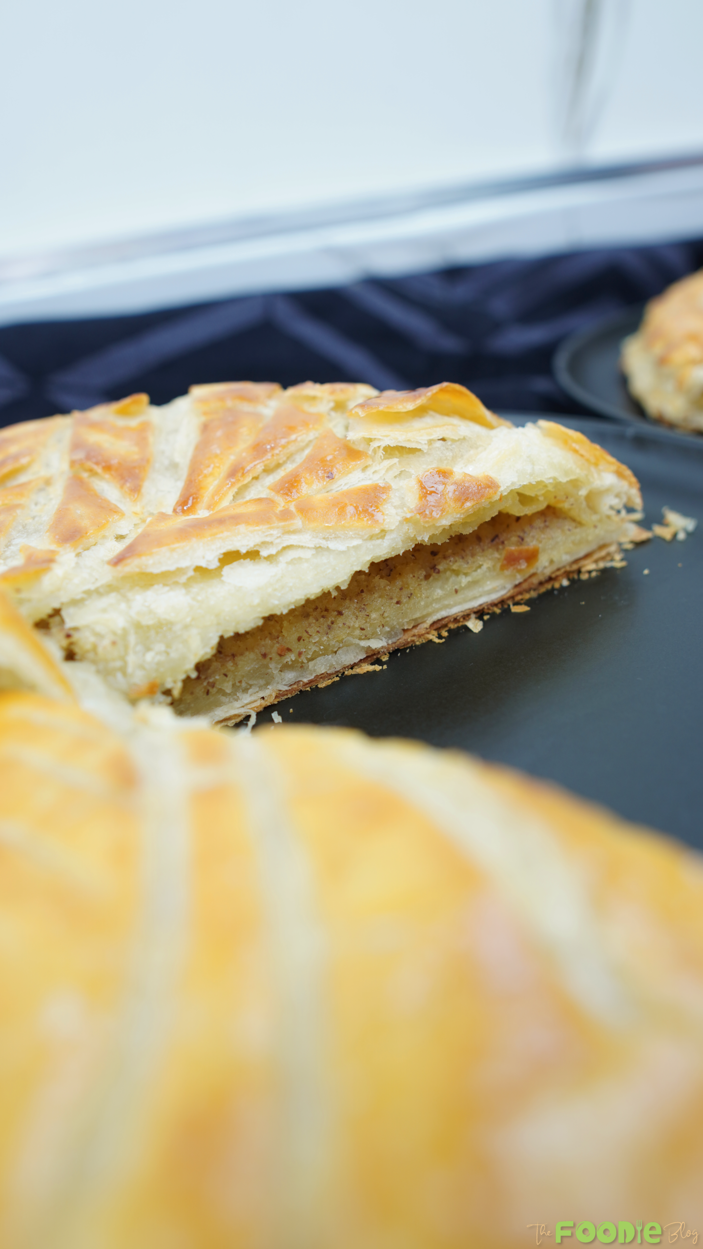 Close-up of a Galette des Rois slice showing flaky puff pastry layers and almond filling on a dark plate