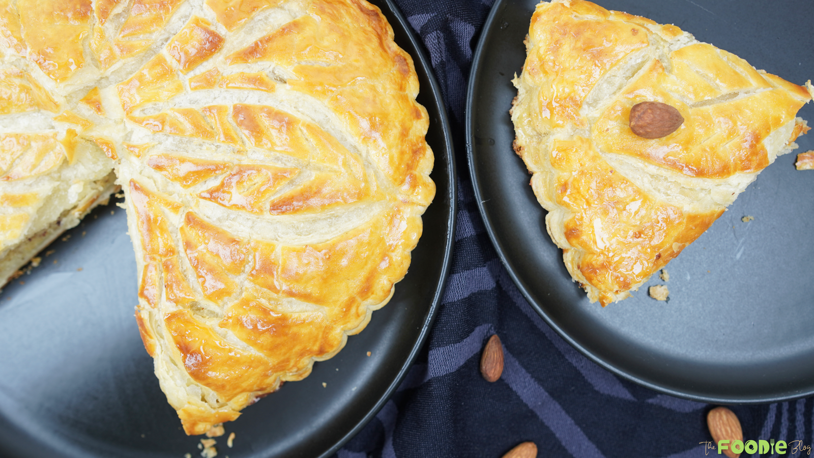 A sliced Galette des Rois with a golden, flaky top served on black plates
