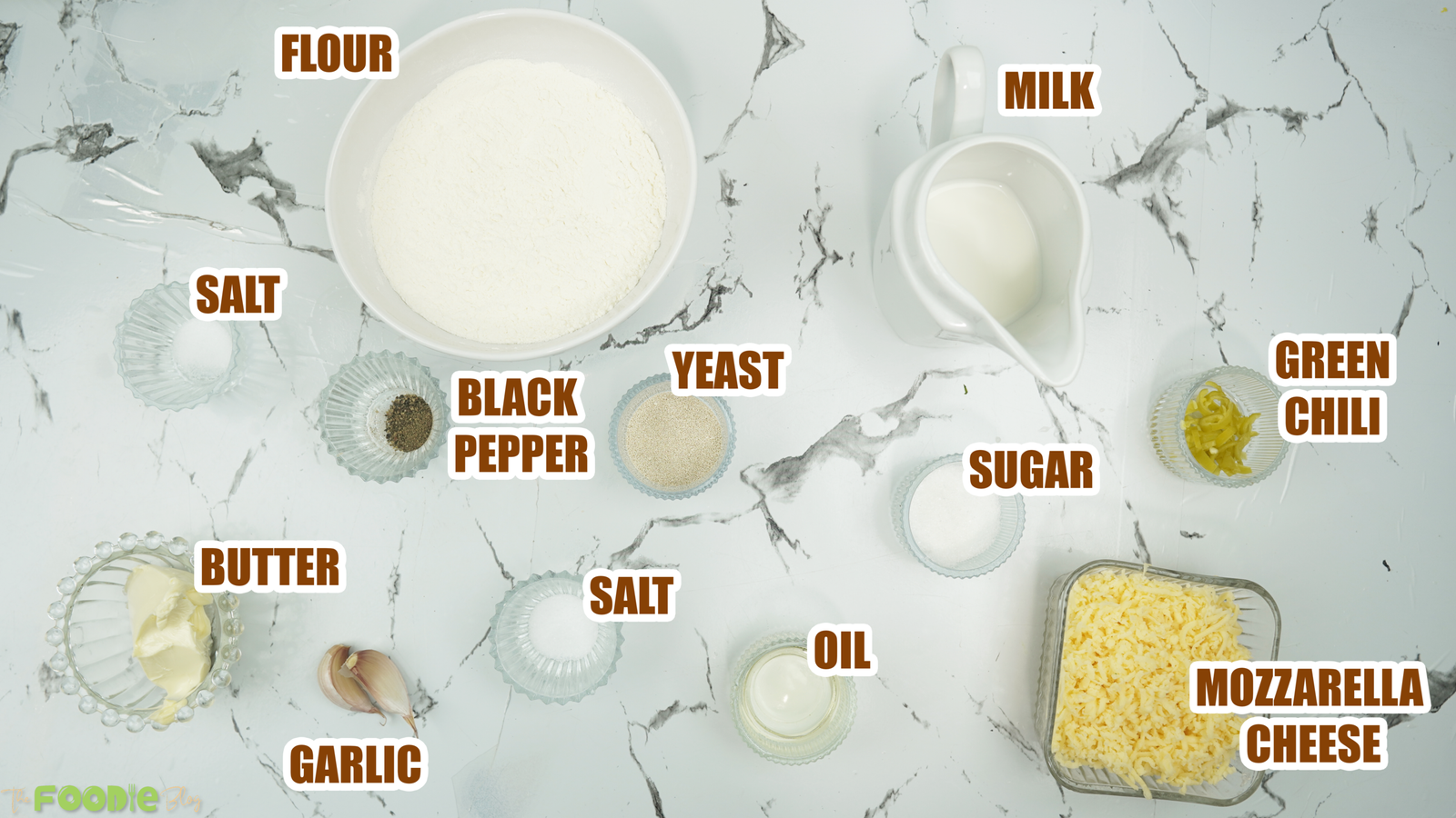 Overhead view of flour, milk, yeast, butter, garlic, mozzarella, and green chili