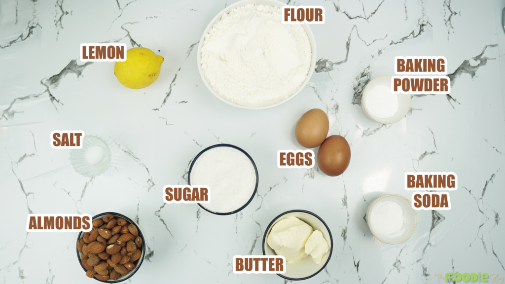 Labeled ingredients for homemade almond biscotti, including flour, sugar, butter, eggs, almonds, lemon, baking powder, baking soda, and salt.