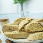 Side view of homemade almond biscotti on a plate with almonds around and a soft blurred background.