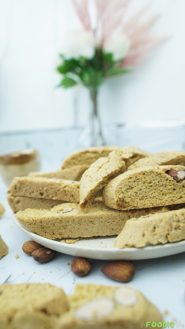 Side view of homemade almond biscotti on a plate with almonds around and a soft blurred background.