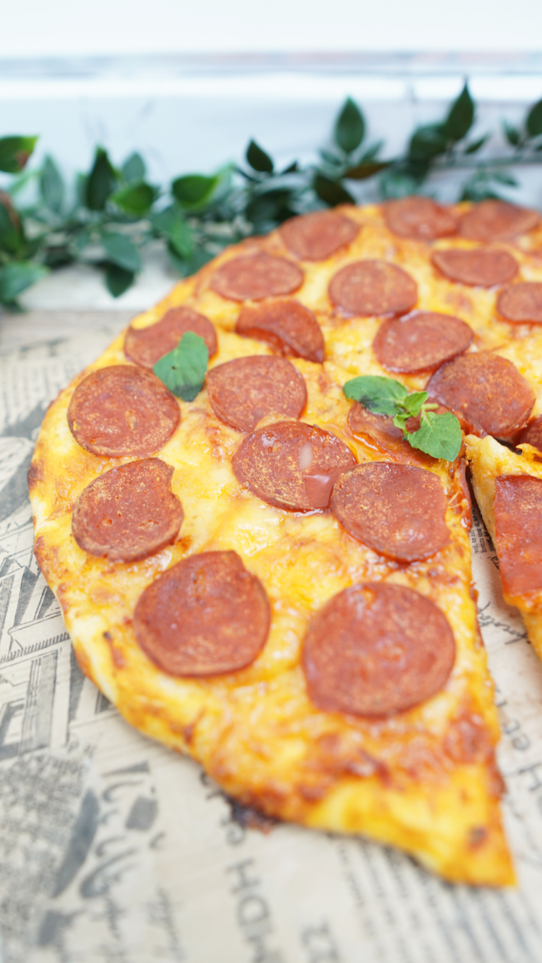 Angled shot of pepperoni pizza with a missing slice and green garnish in the background