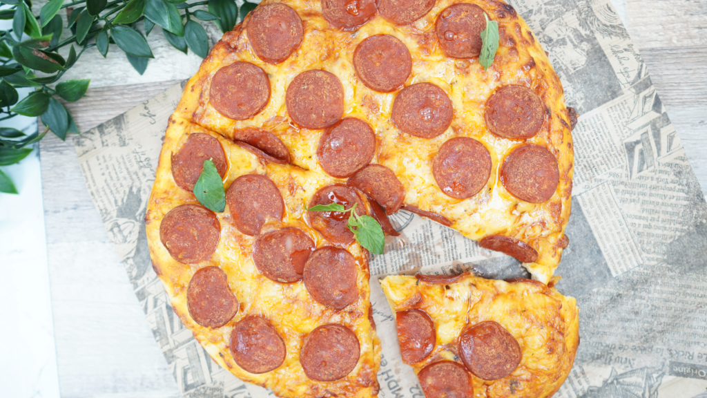 Overhead view of a whole pepperoni pizza with one slice removed on parchment paper