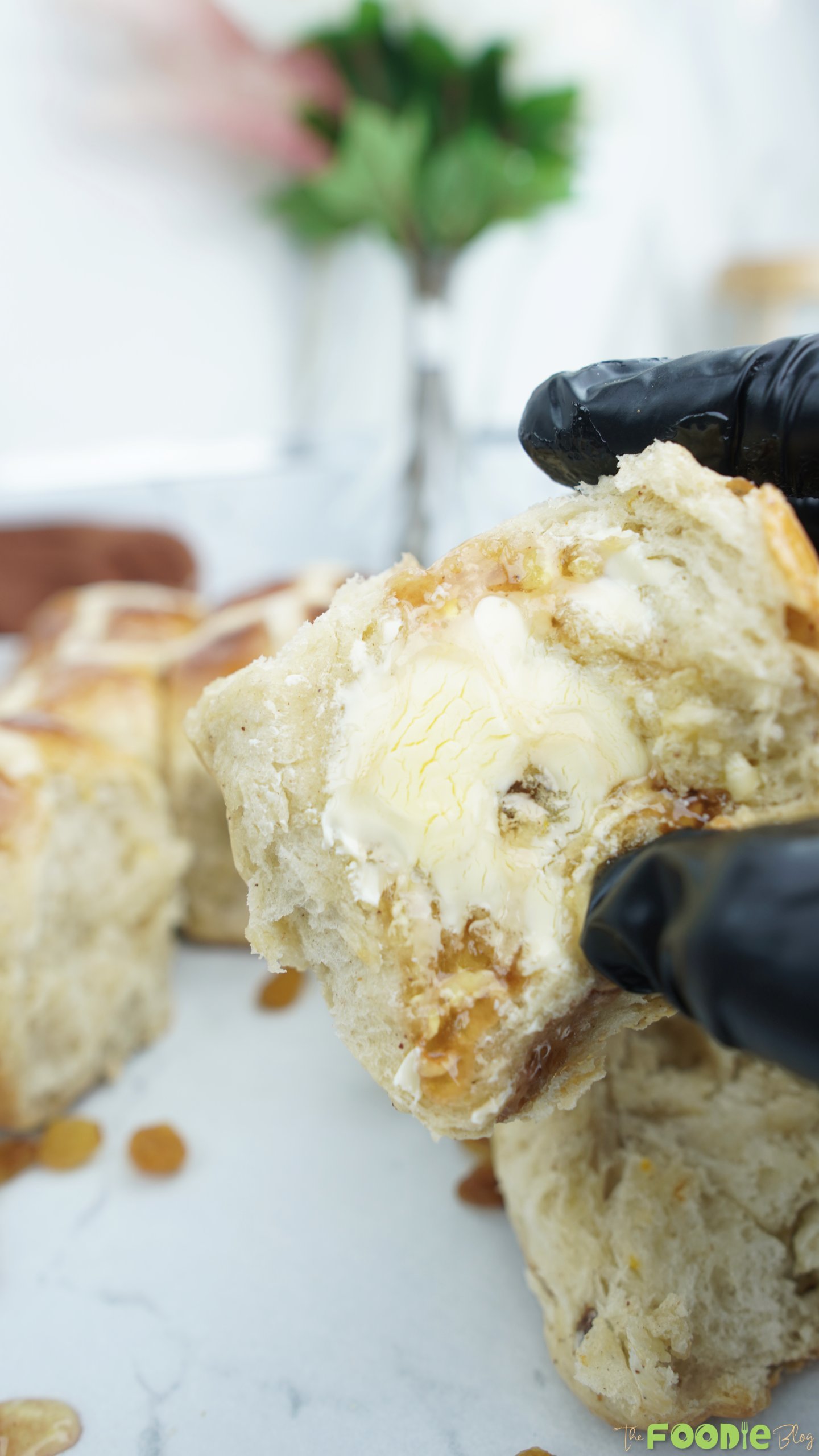 Hand holding a buttered piece of hot cross bun with raisins in the crumb
