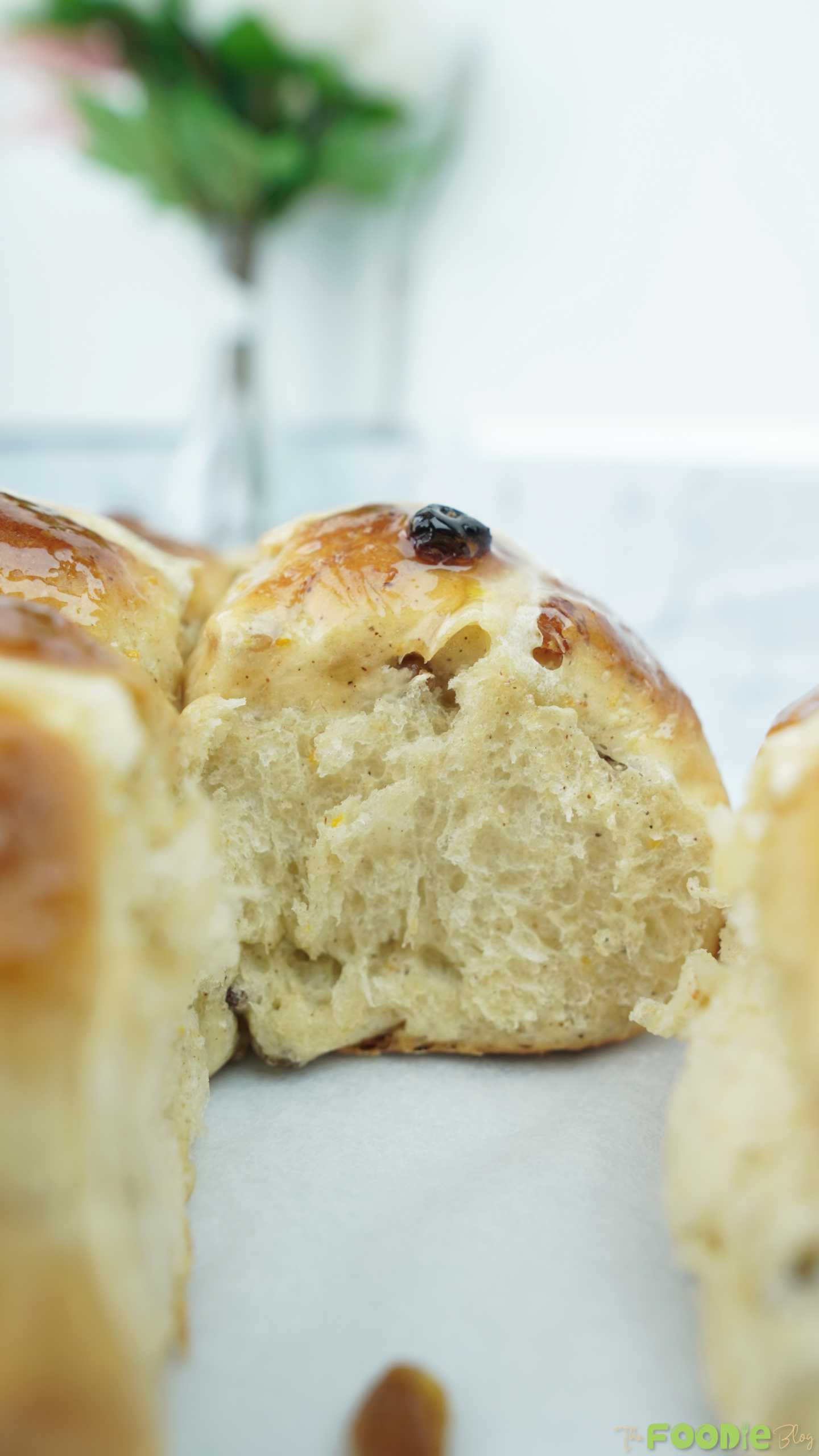 Close-up of a torn hot cross bun showing raisins and a shiny glaze on top