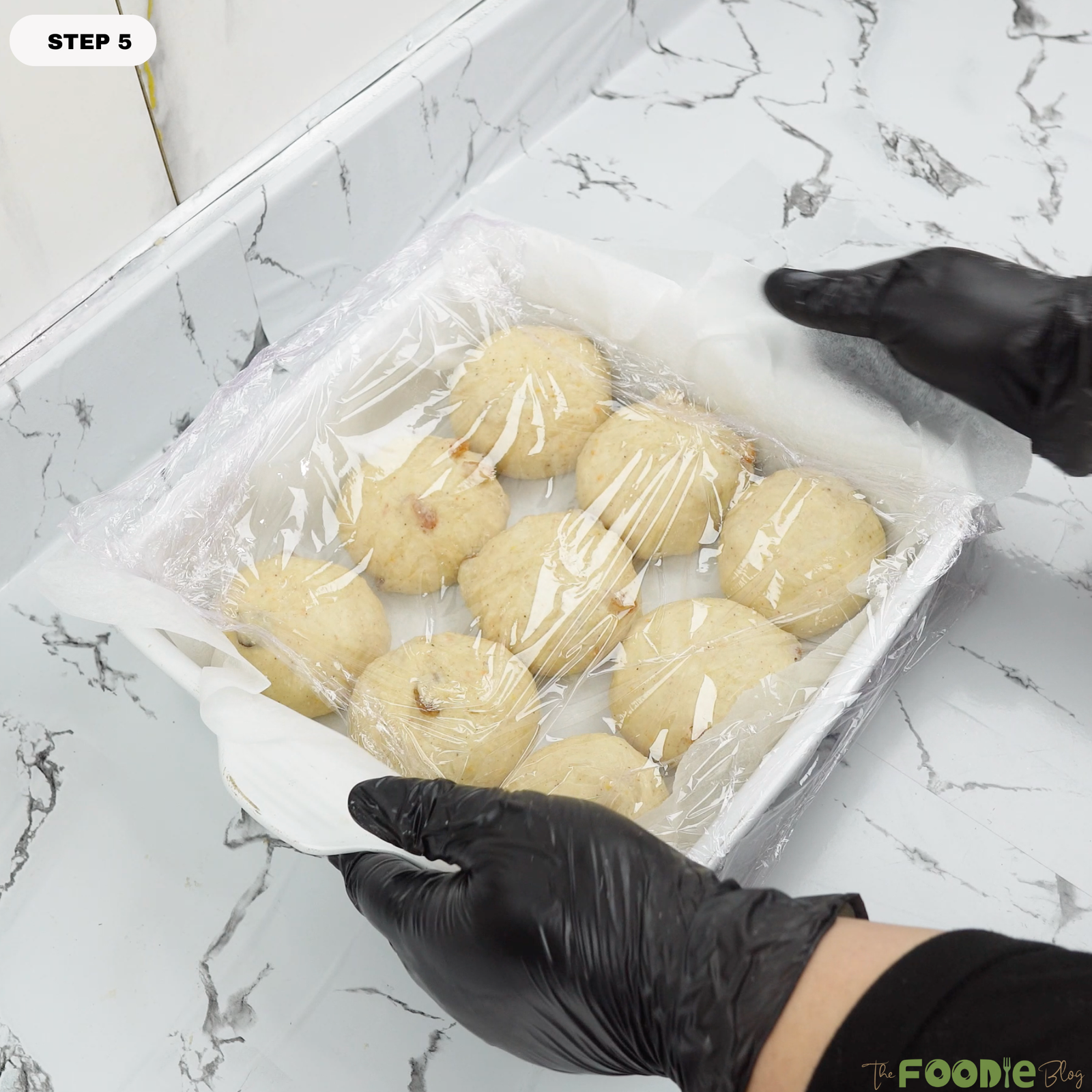Baking pan filled with shaped buns covered with plastic wrap for second rise