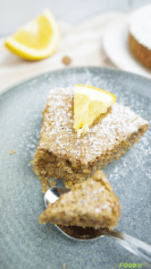 A slice of Italian Almond Cake dusted with powdered sugar on a plate with a citrus wedge