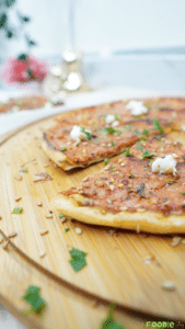 Close-up of Lebanese flatbread pizza topped with sesame seeds, herbs, and goat cheese on a wooden board