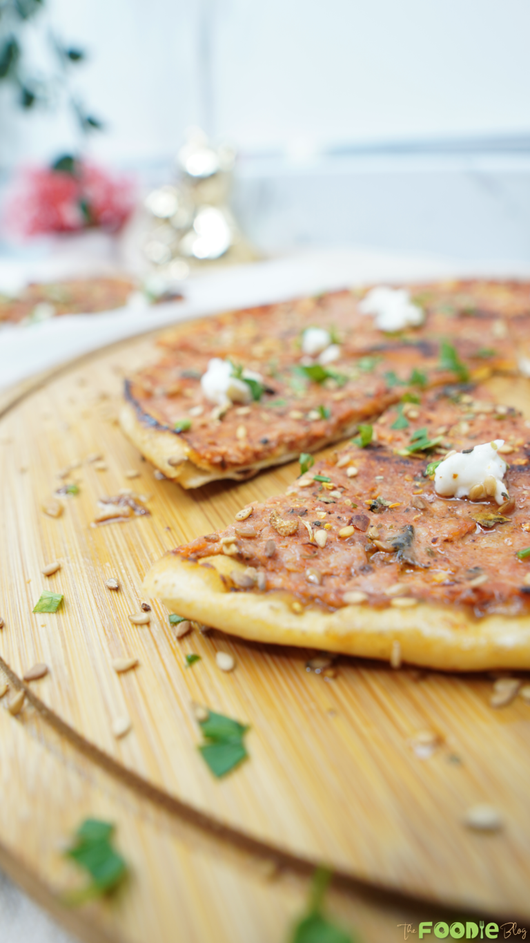 Close-up of Lebanese flatbread pizza topped with sesame seeds, herbs, and goat cheese on a wooden board