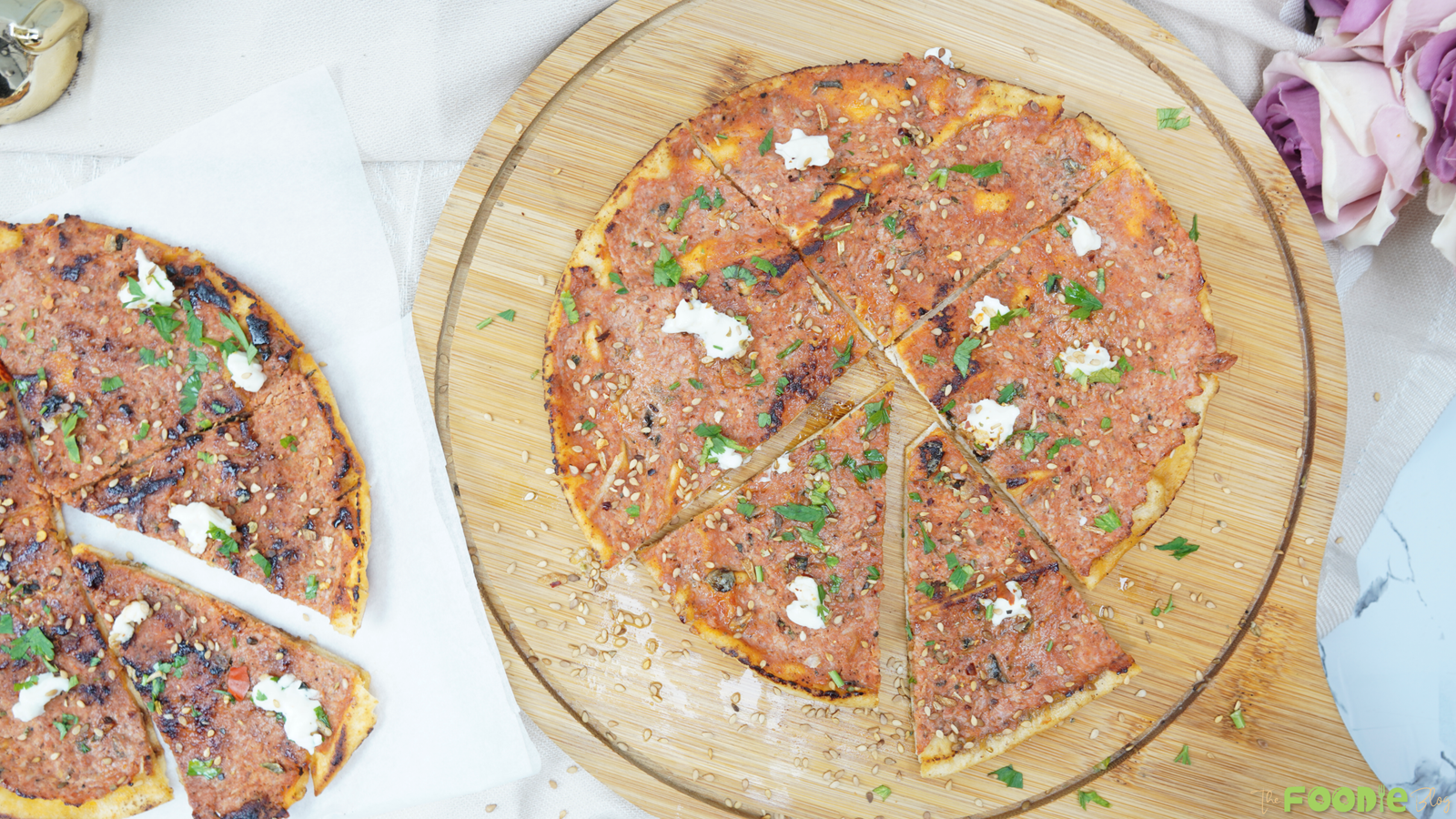 Overhead view of sliced Lebanese flatbread pizza topped with herbs, sesame seeds, and small dots of goat cheese