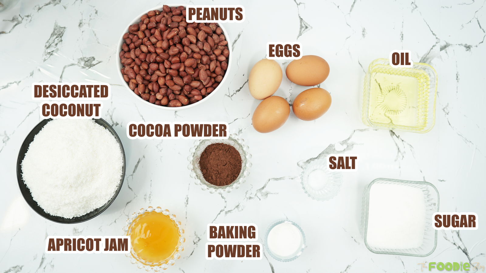 Overhead view of peanuts, eggs, cocoa powder, coconut, sugar, oil, baking powder, salt, and apricot jam