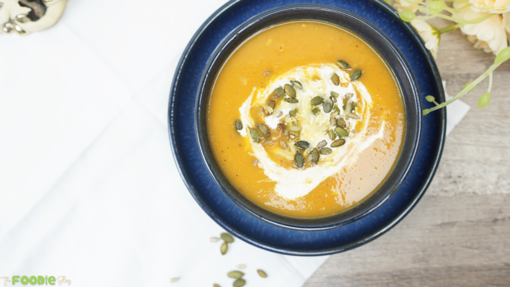Creamy roasted veggie soup in a blue bowl topped with crème fraîche and pepitas