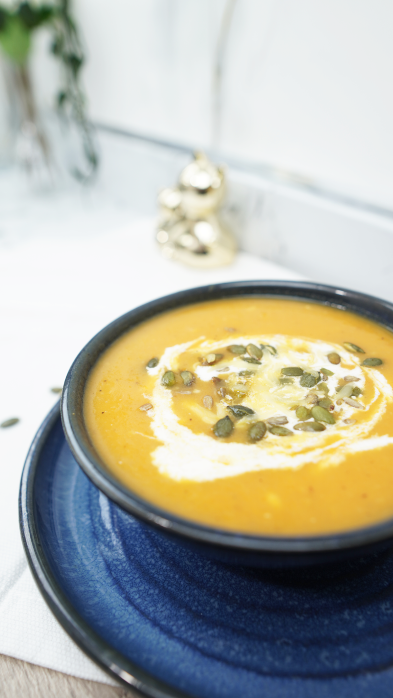 Oven roasted veggie soup served in a dark bowl on a blue plate with crème fraîche and pepitas