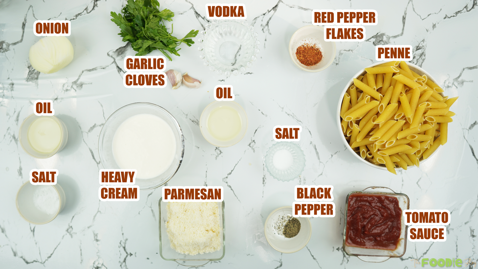 Flat lay of penne, heavy cream, tomato sauce, vodka, Parmesan, onion, garlic, and seasonings on a marble surface