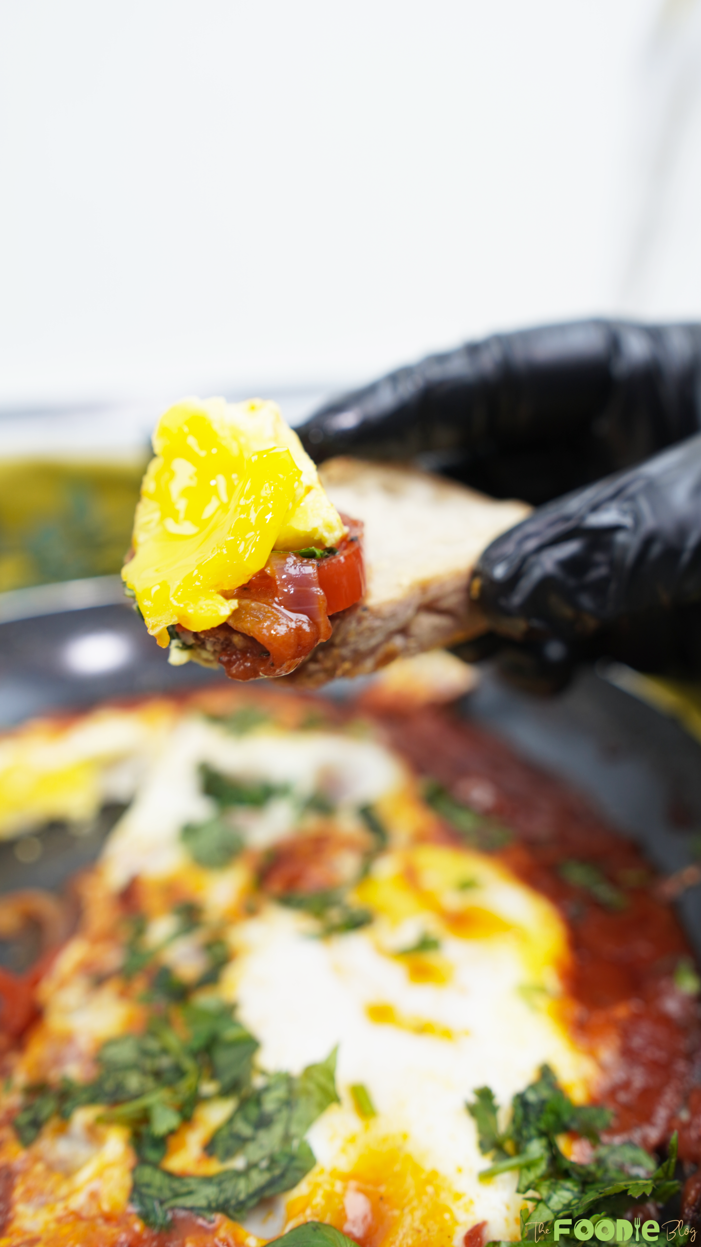 A bite of shakshuka on a piece of bread with runny yolk and tomato sauce