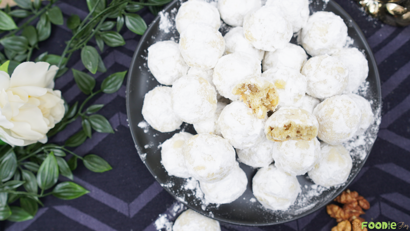 Overhead view of a plate piled with snowball cookies coated in powdered sugar with a few cookies broken open
