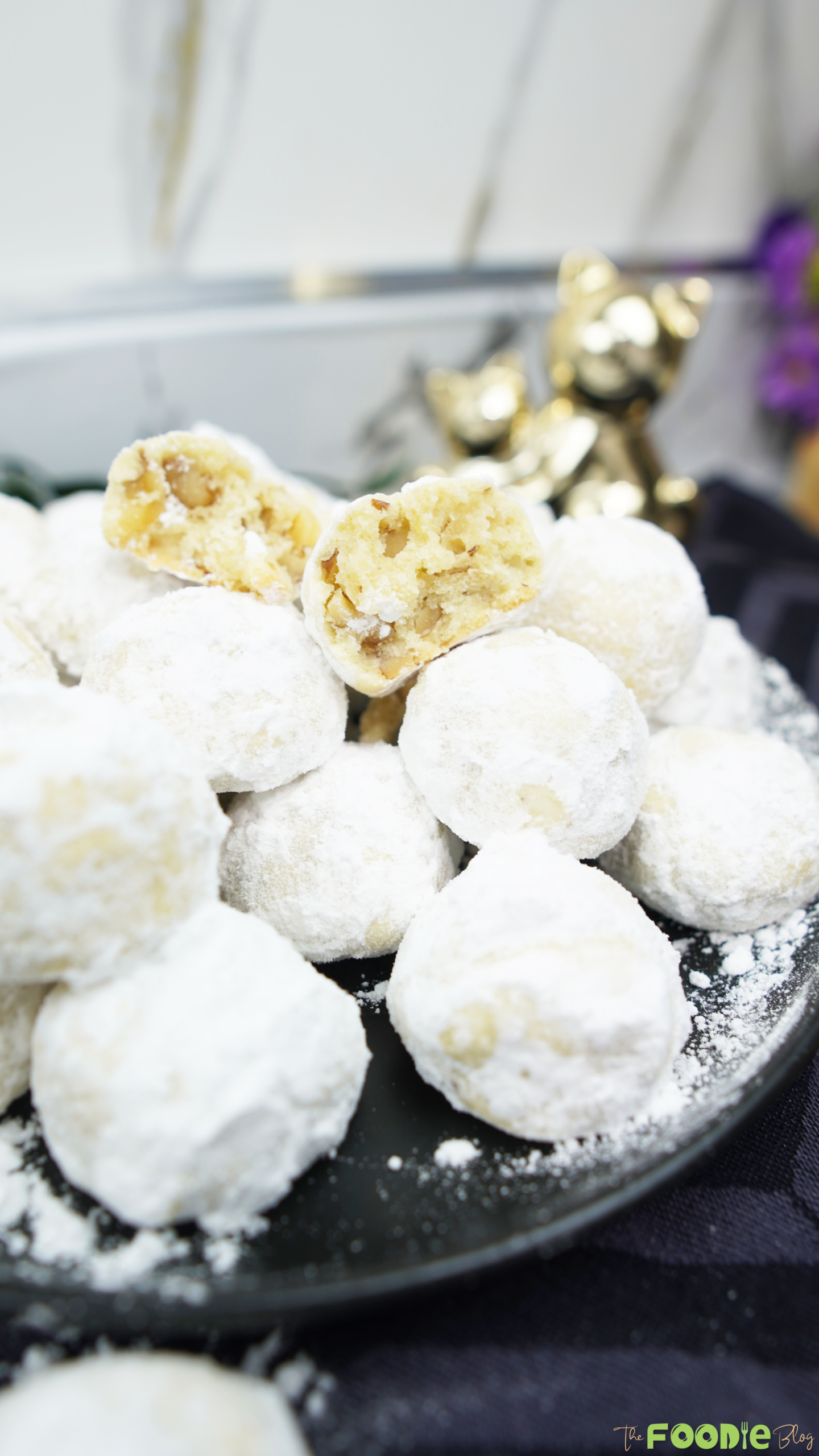 Snowball cookies stacked on a plate with a broken cookie on top showing the soft inside and chopped walnuts