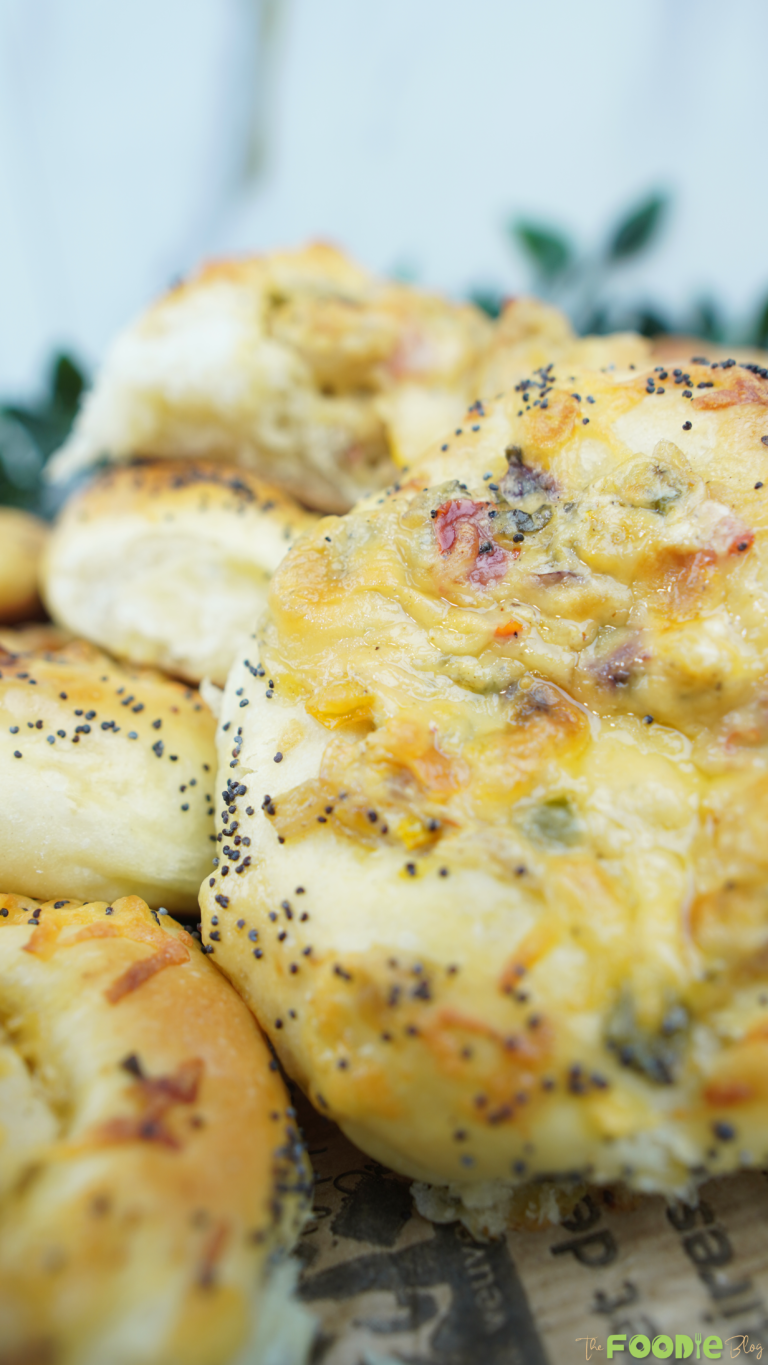 Close-up of a soft cheese pizza bun showing melted cheese, veggies, and poppy seeds on the crust