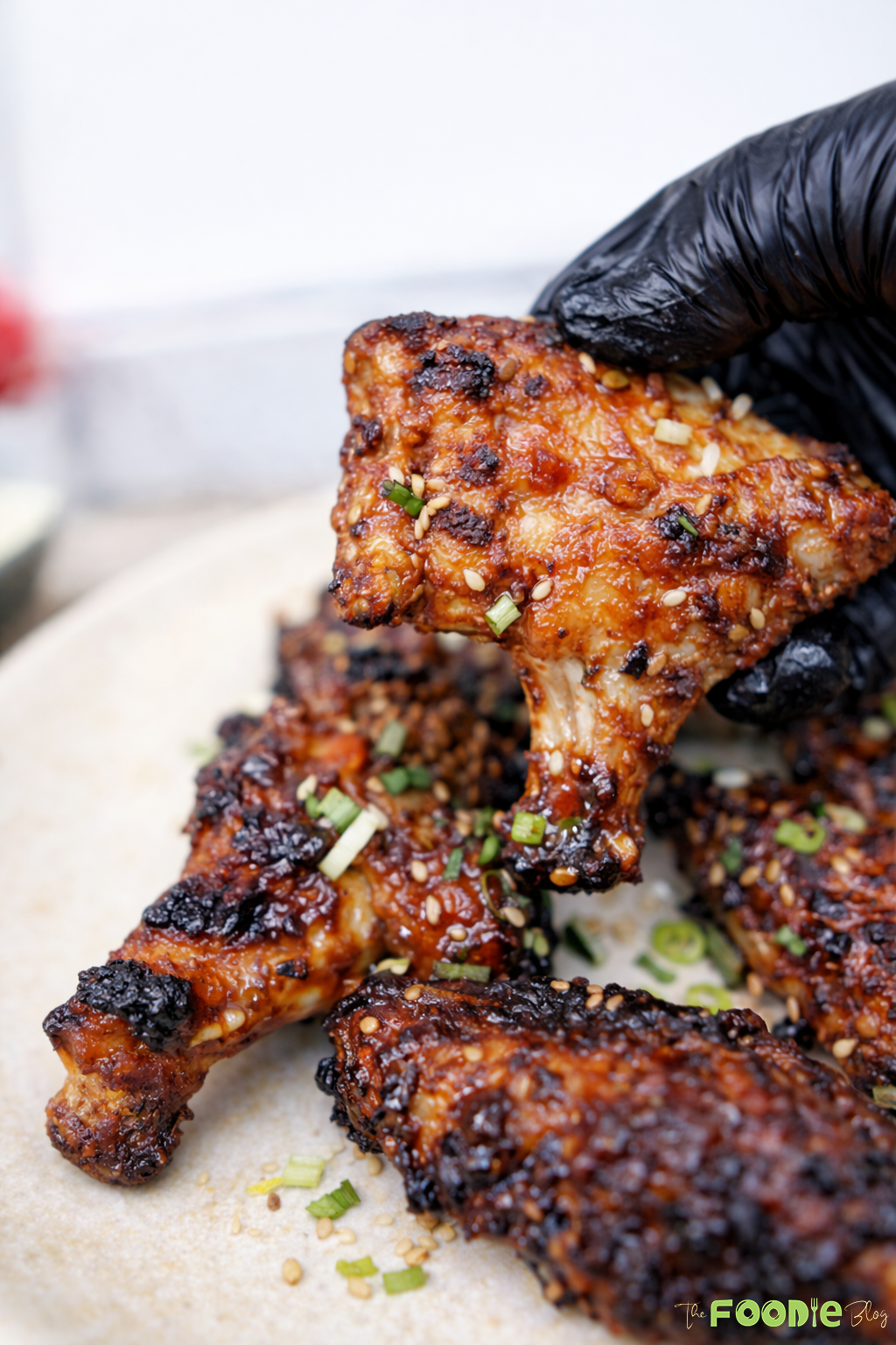 Close-up of sticky Chinese chicken wings with a thick glossy glaze, sesame seeds, and scallions.